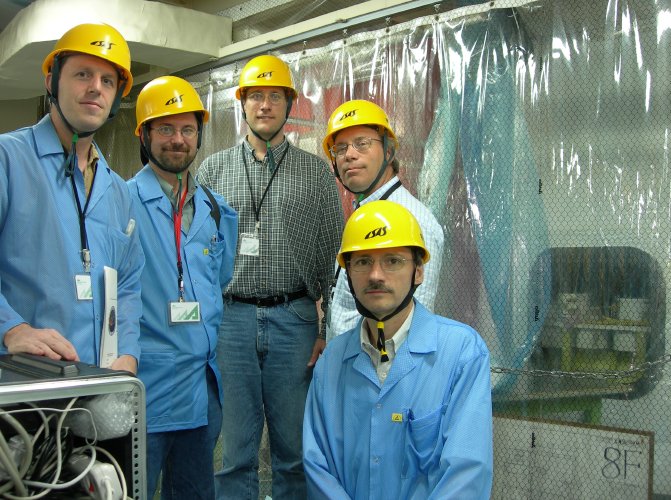5 serious-faced men stand in front of a translucent curtain, behind which the round surface of the rocket is foggily visible. (101K JPEG)