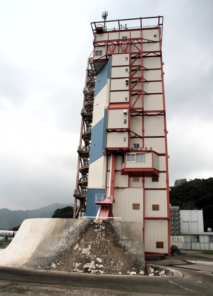 The launch tower, um, towers in the background against a sky the color of television, tuned to a dead channel.  In the foreground the concrete curve of the flame deflector is discolored and spalled from the flames of multiple rockets. (61K JPEG)